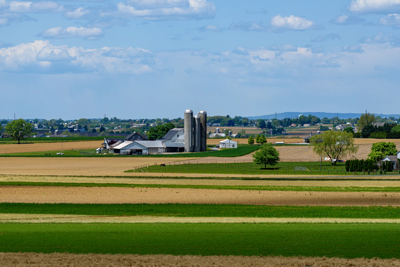 Farmland with a grain silo and farm buildings under a partly cloudy sky